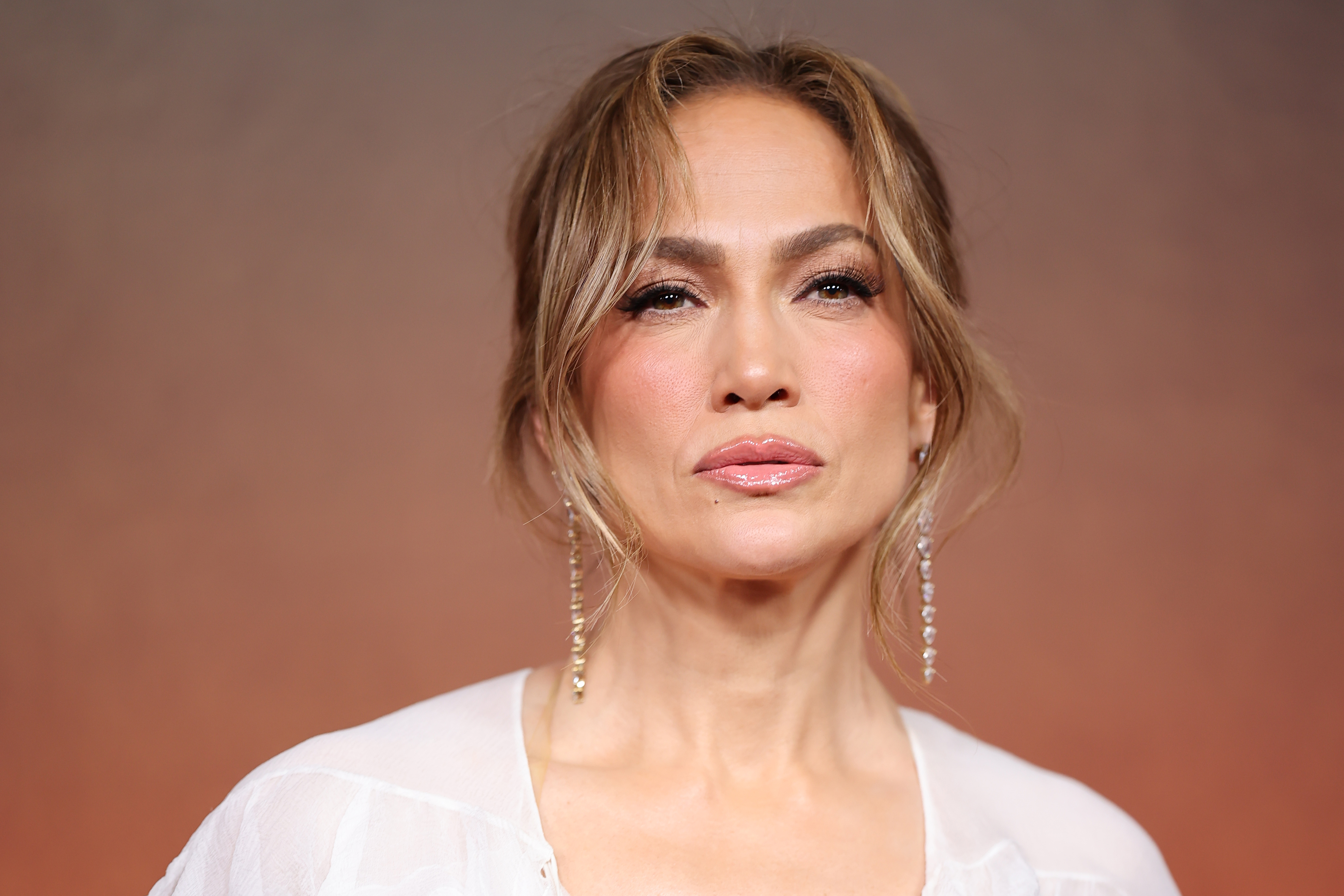 Jennifer Lopez in a white outfit with long, dangling earrings, posing for a photo