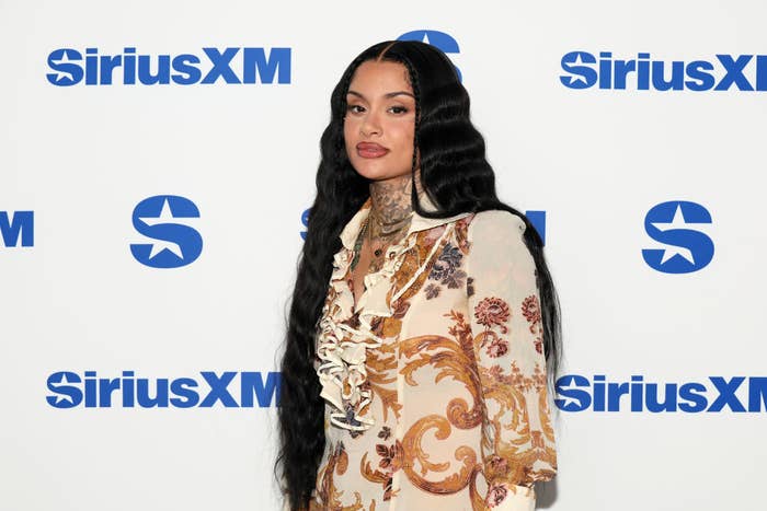 Kehlani at SiriusXM event, wearing a patterned dress with lace detailing and long, wavy hair