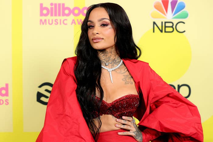 Kehlani on the red carpet at the Billboard Music Awards, wearing a red sequin strapless top and matching red shawl, with visible chest and arm tattoos