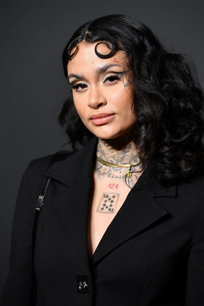 Kehlani with wavy hair in a black blazer, showing visible tattoos on her neck and chest
