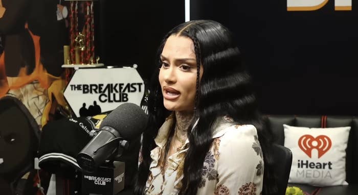 Kehlani at The Breakfast Club radio interview, speaking into a microphone. Background shows The Breakfast Club logo and iHeart Media pillow