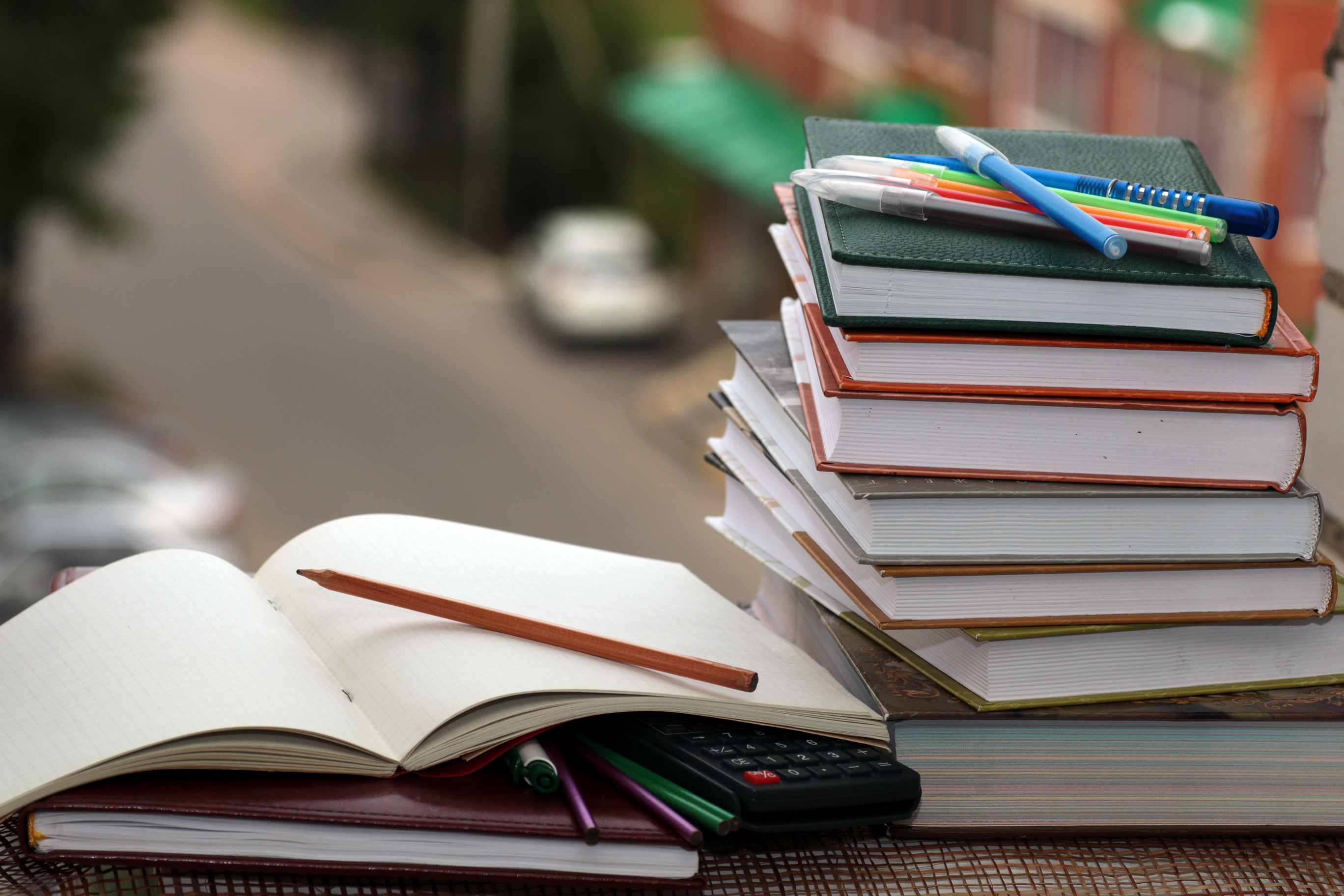 Open notebooks, a stack of books, pens, pencils, and a calculator on a table, suggesting a workspace or study area. No people in the image