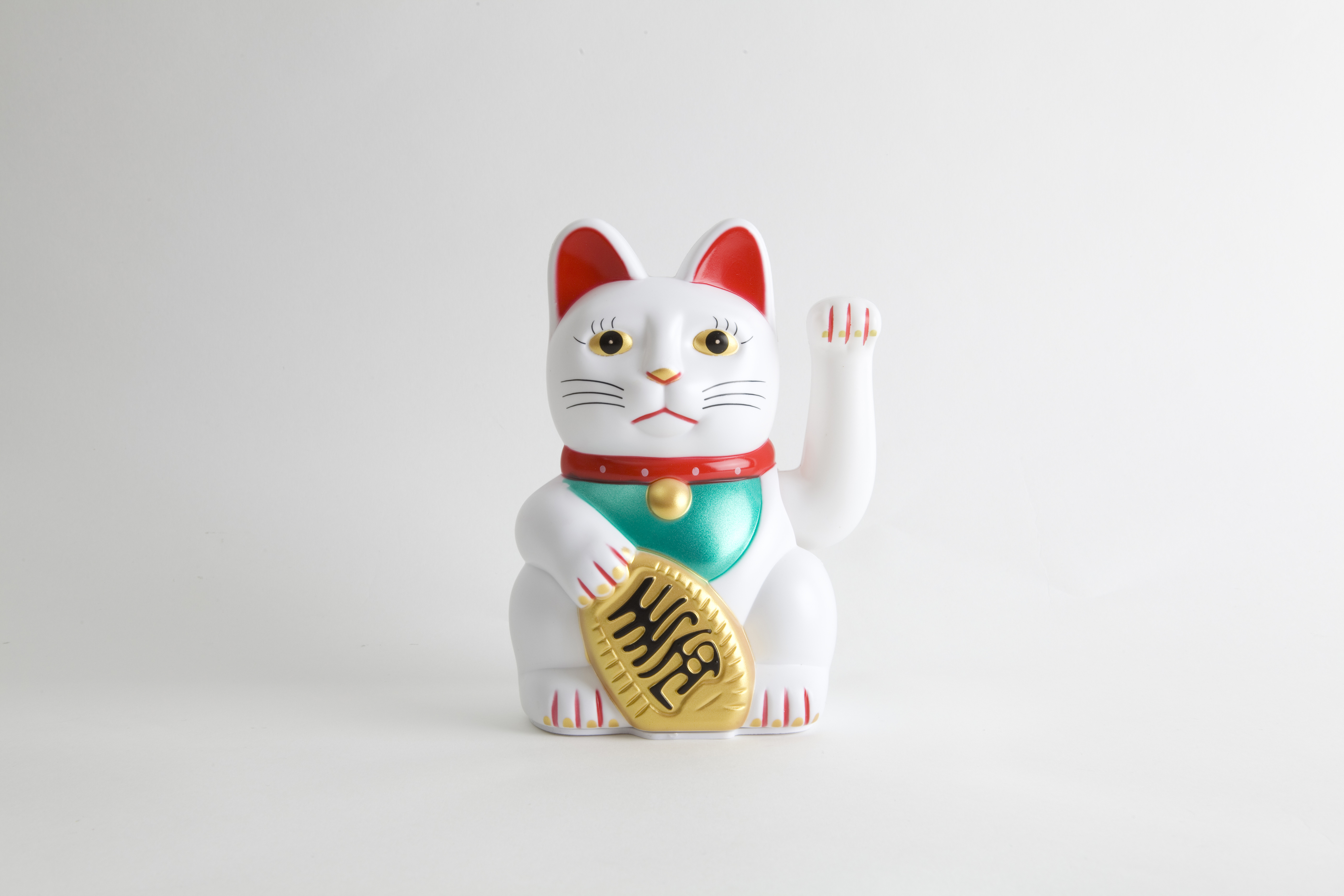 A Japanese maneki-neko (beckoning cat) figurine with its paw raised, wearing a collar and a bell, holding a gold coin