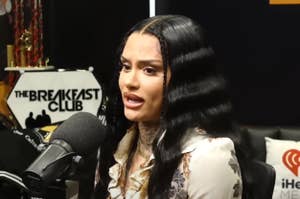 Kehlani at The Breakfast Club radio show, speaking into a microphone. She is wearing a floral blouse and has long, wavy hair