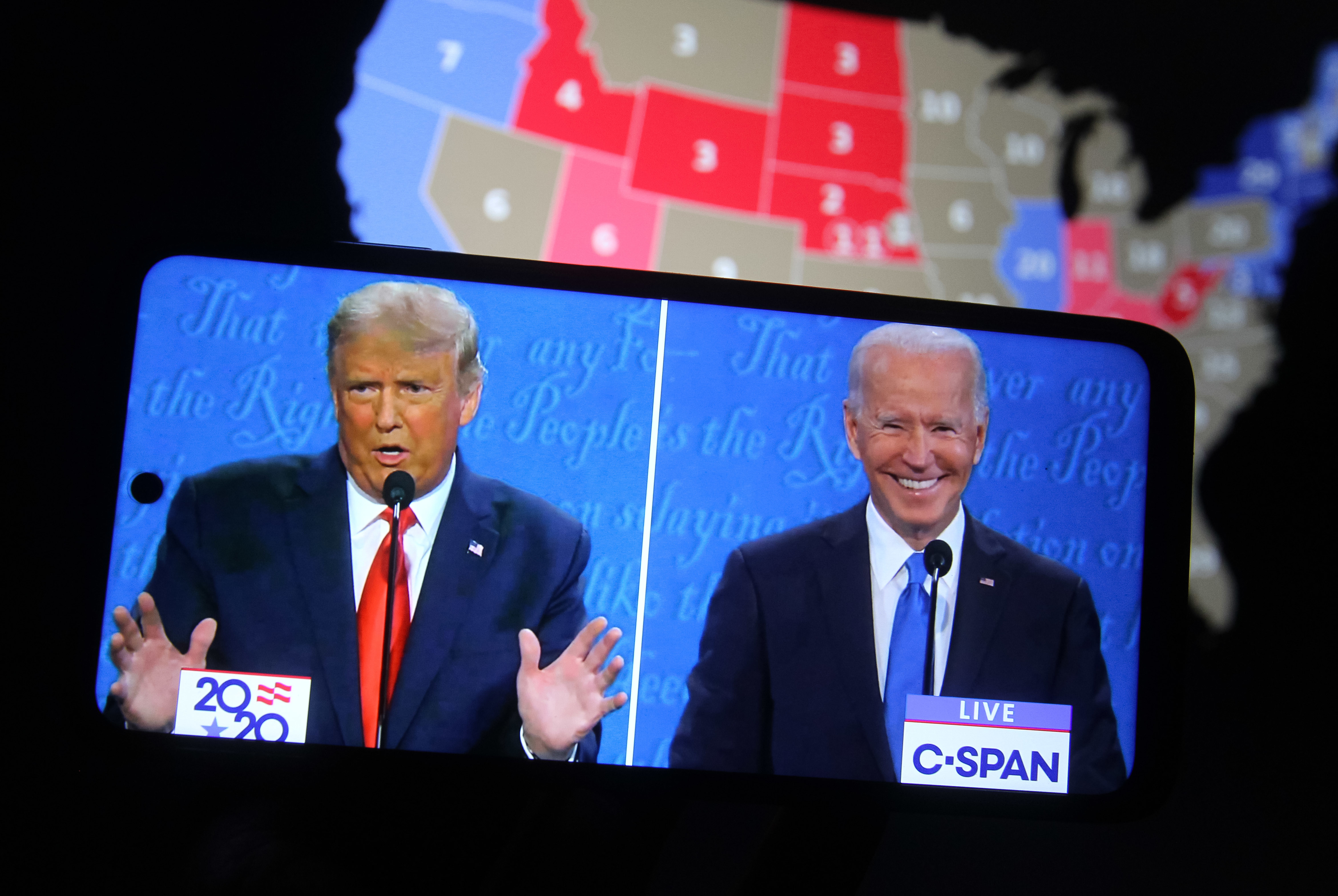 Donald Trump and Joe Biden during a televised debate, with a map of the United States in the background