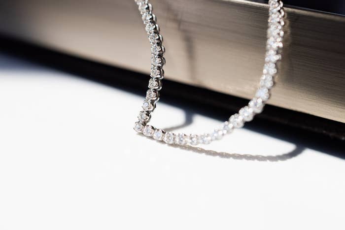 Close-up image of a diamond tennis bracelet draped over the edge of a jewelry box, reflecting light