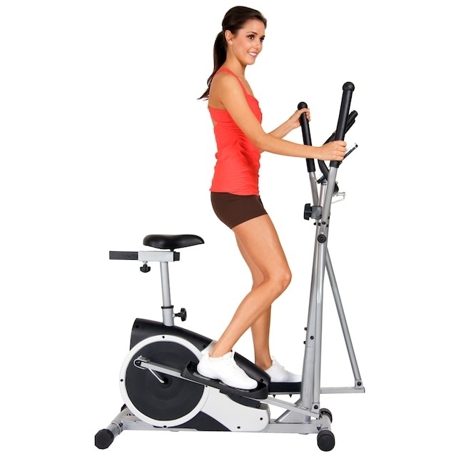 Model using an elliptical bike in an indoor setting, dressed in fitness attire with a sleeveless top and shorts, smiling ahead