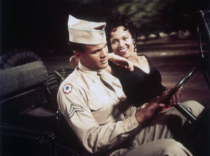 Harry Belafonte in military uniform and Dorothy Dandridge in a sleeveless dress sitting in a vehicle. Dandridge leans on Belafonte&#x27;s shoulder, both smiling