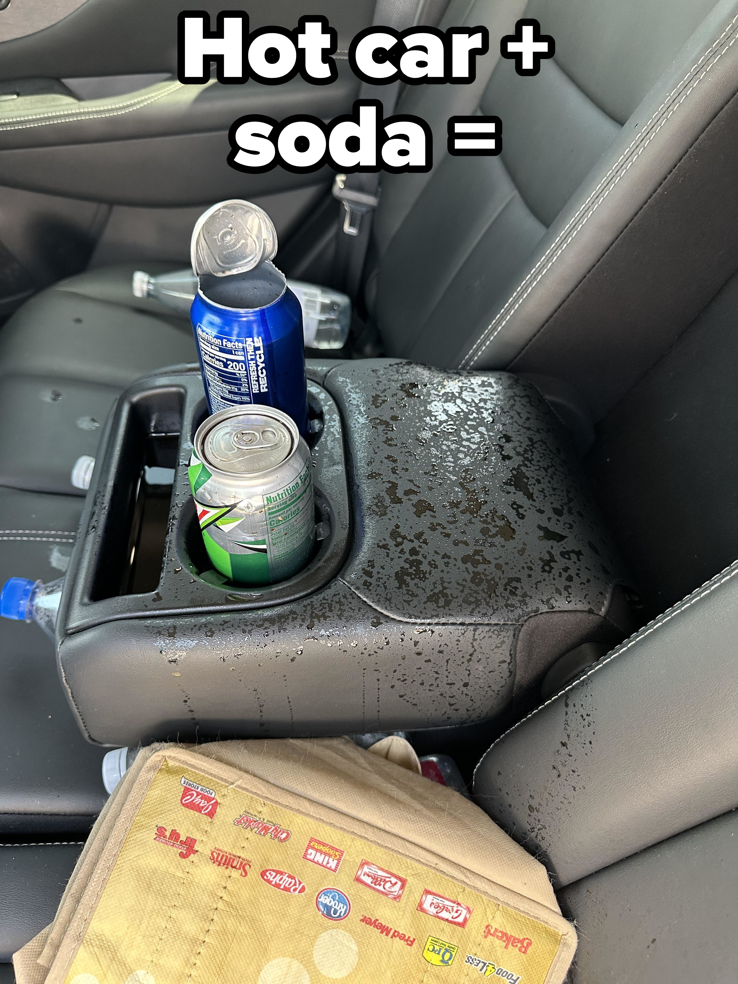 Two soda cans, one on its side and spilled onto the car&#x27;s center console, with water bottles and a tote bag nearby on the backseat