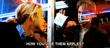 Matt Damon holds a paper against a window, showing it to a blonde man, with the text &quot;How you like them apples?&quot; at the bottom