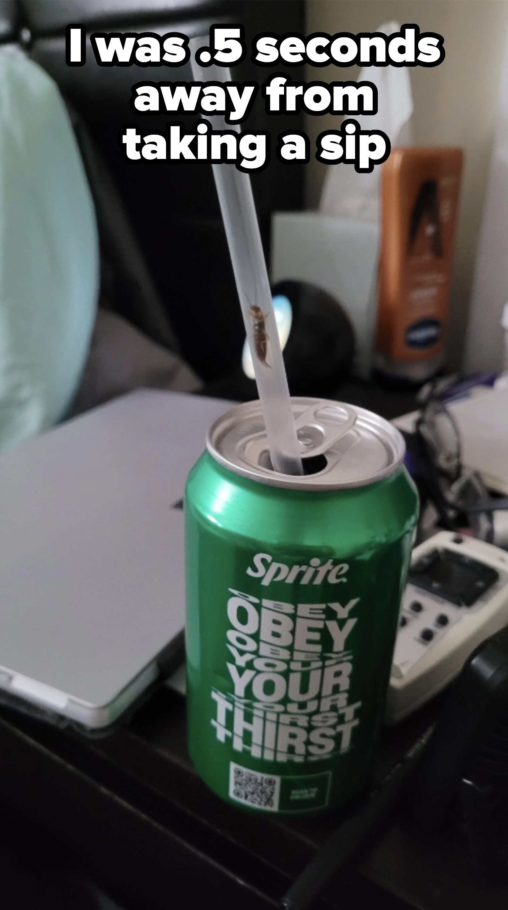A green Sprite can with a straw. There is an insect crawling inside the straw. The can is on a desk with various items like a tissue box and electronic devices
