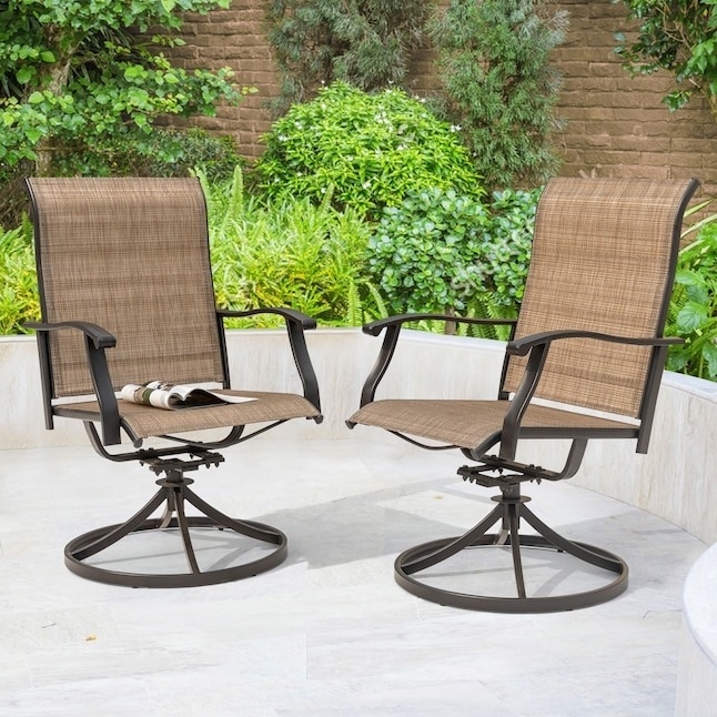 Two patio chairs with armrests and a magazine on one, set on a stone patio with lush greenery in the background
