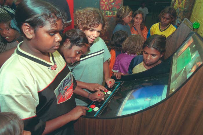 A group of children are gathered around and playing an arcade game machine in a lively, indoor setting.