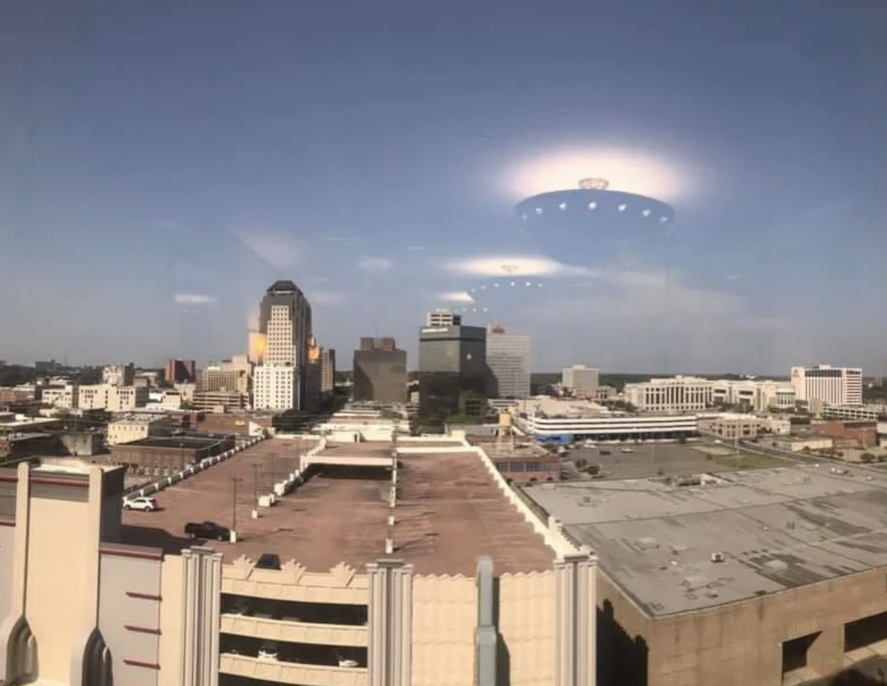 City skyline view from above with buildings and clear sky, reflecting lights resembling UFOs in the window