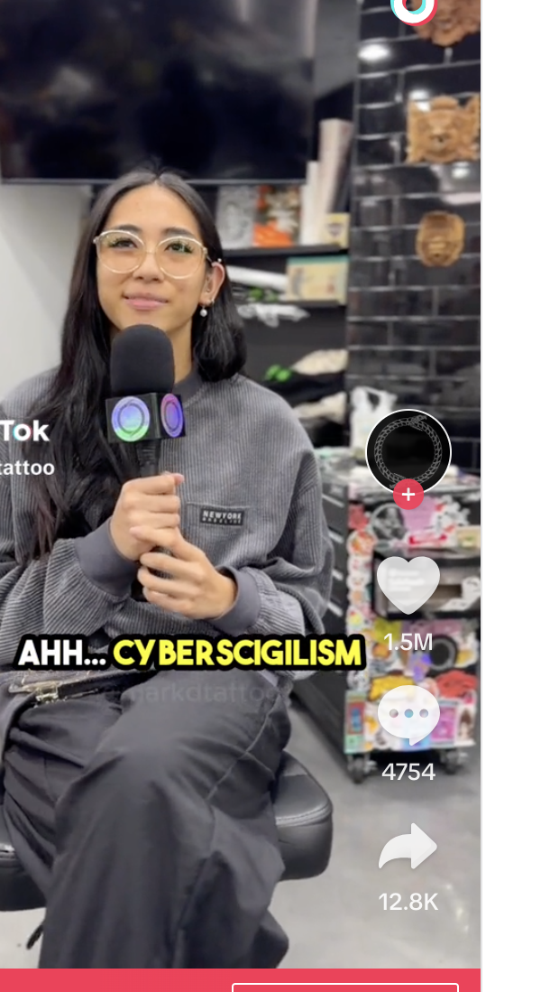 Woman in glasses and a gray sweater speaks into a microphone in a TikTok video with the caption &quot;AHH... CYBERSCIGILISM.&quot; TikTok logo visible on screen