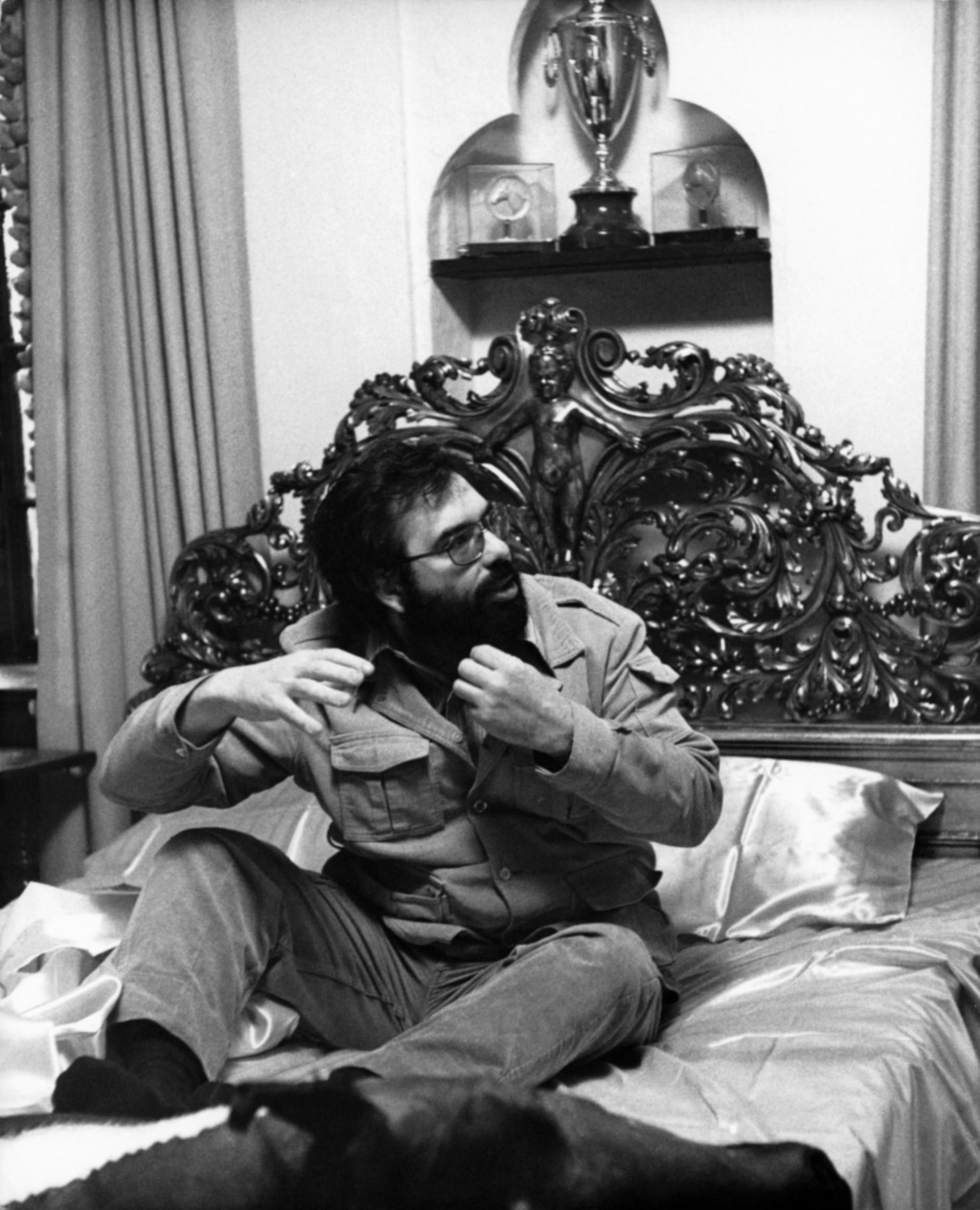 Francis Ford Coppola in a detailed ornate bed, adjusting his beard