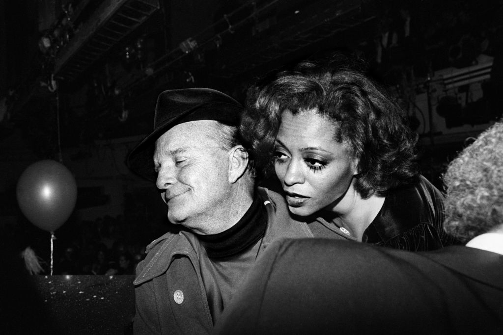 Truman Capote wearing a hat and coat, and Diana Ross leaning towards him, both at a social event