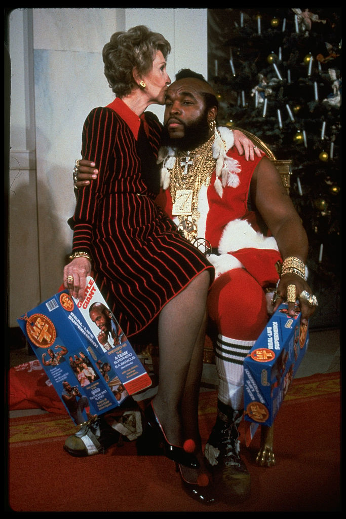 Nancy Reagan kisses Mr. T, dressed as Santa, while they hold boxes of Mr. T cereal in front of a Christmas tree