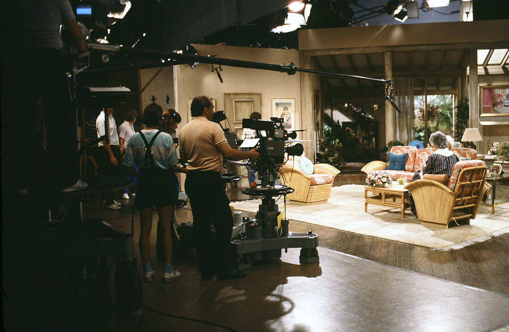 Filming crew on the set of &quot;The Golden Girls&quot; with actors rehearsing a scene in the living room set. Camera and boom operators are preparing for a shoot