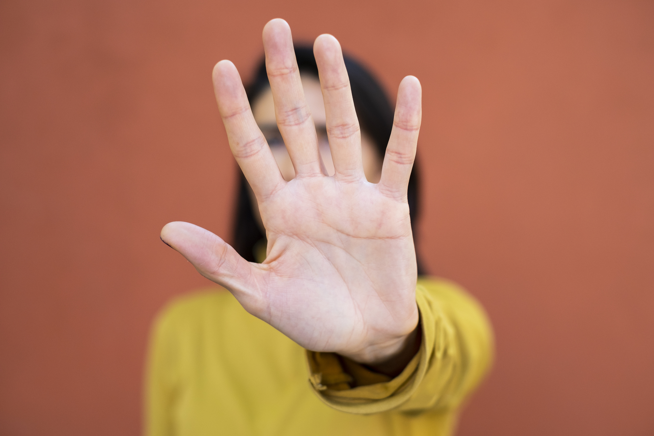 A person with an outstretched hand blocking their face, fingers spread wide apart