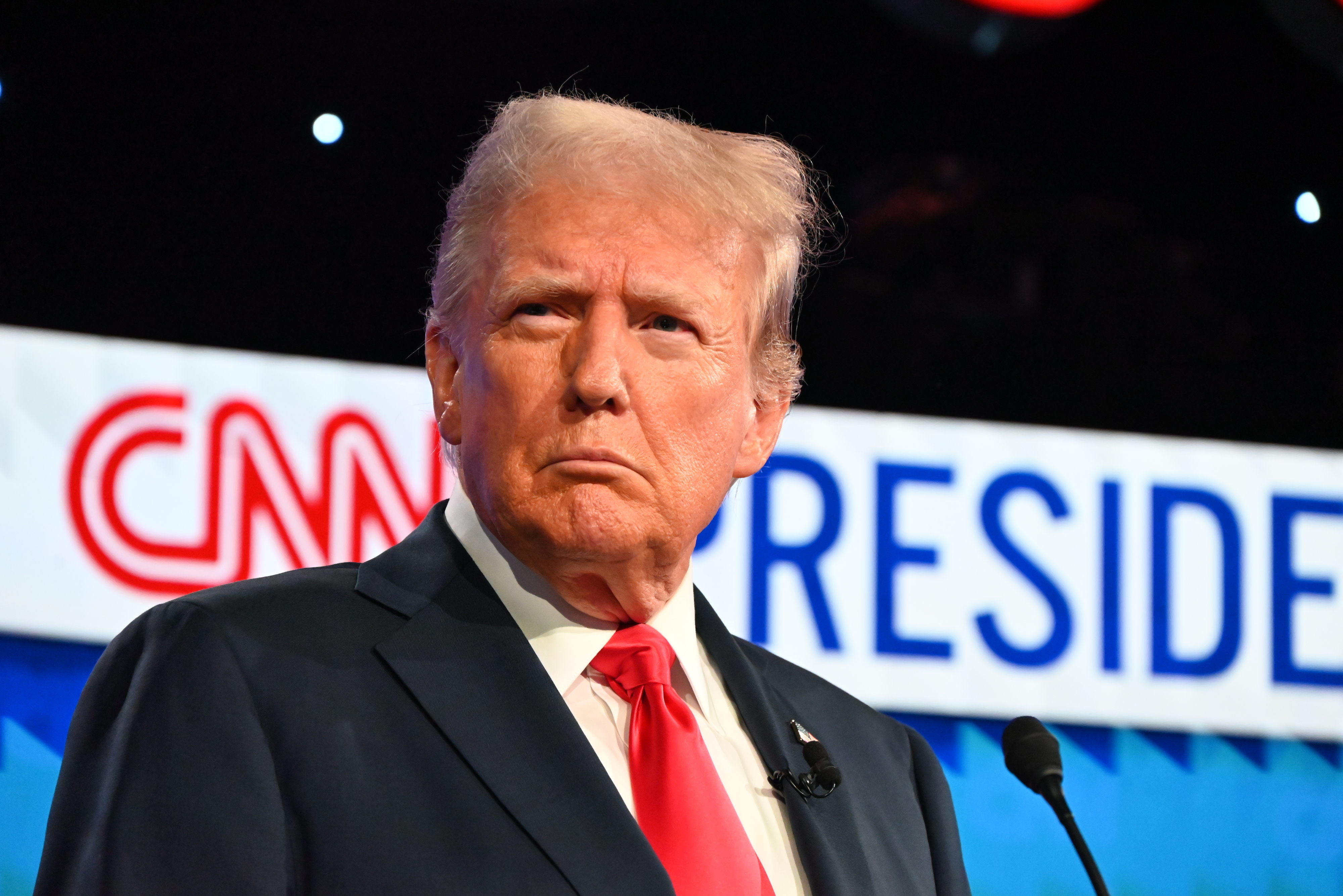 Donald Trump stands in front of a &quot;CNN President&quot; sign, wearing a suit with a red tie, at a televised event