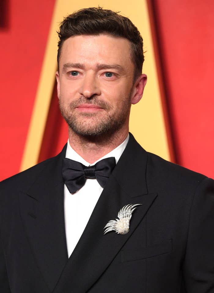 Justin Timberlake wearing a suit with a bow tie and a decorative pin, posing on the red carpet