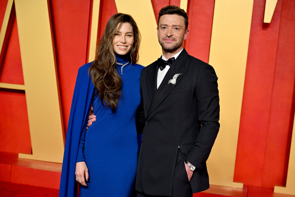 Jessica Biel and Justin Timberlake pose together on the red carpet. Jessica wears a long-sleeved, floor-length dress with a cape, while Justin wears a suit and bow tie