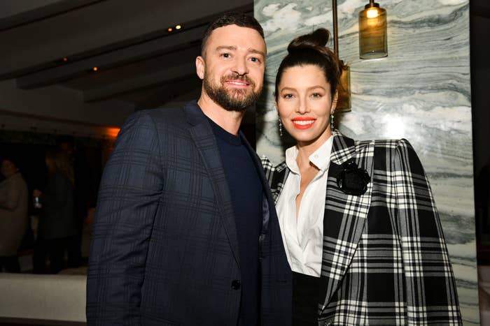 Justin Timberlake in a plaid blazer and Jessica Biel in a black and white checkered jacket smile at a formal indoor event