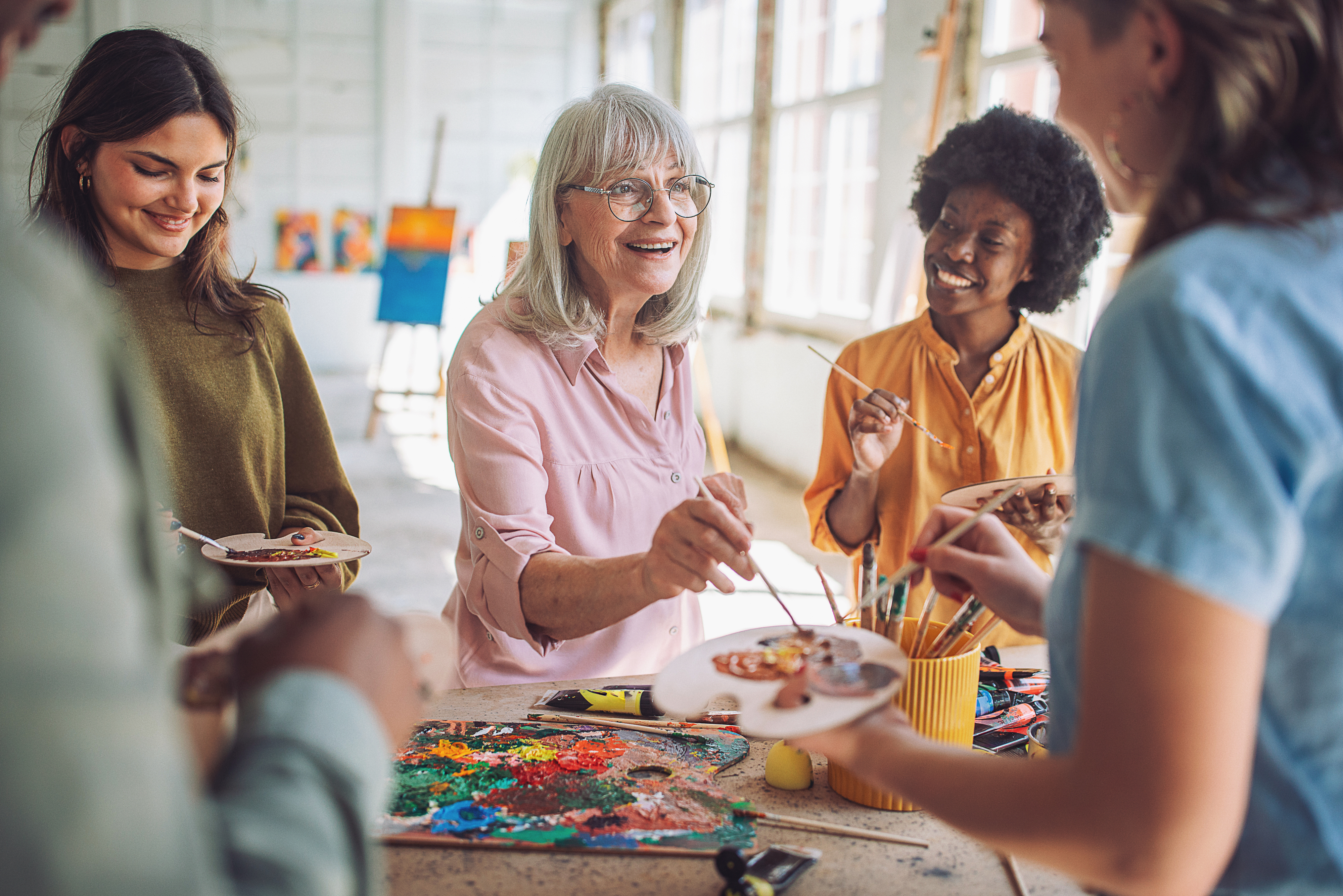 Group of women, including older woman with glasses, painting and smiling in an art studio