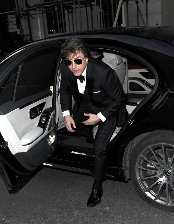 Tom Cruise steps out of a luxury sedan wearing a black tuxedo and sunglasses
