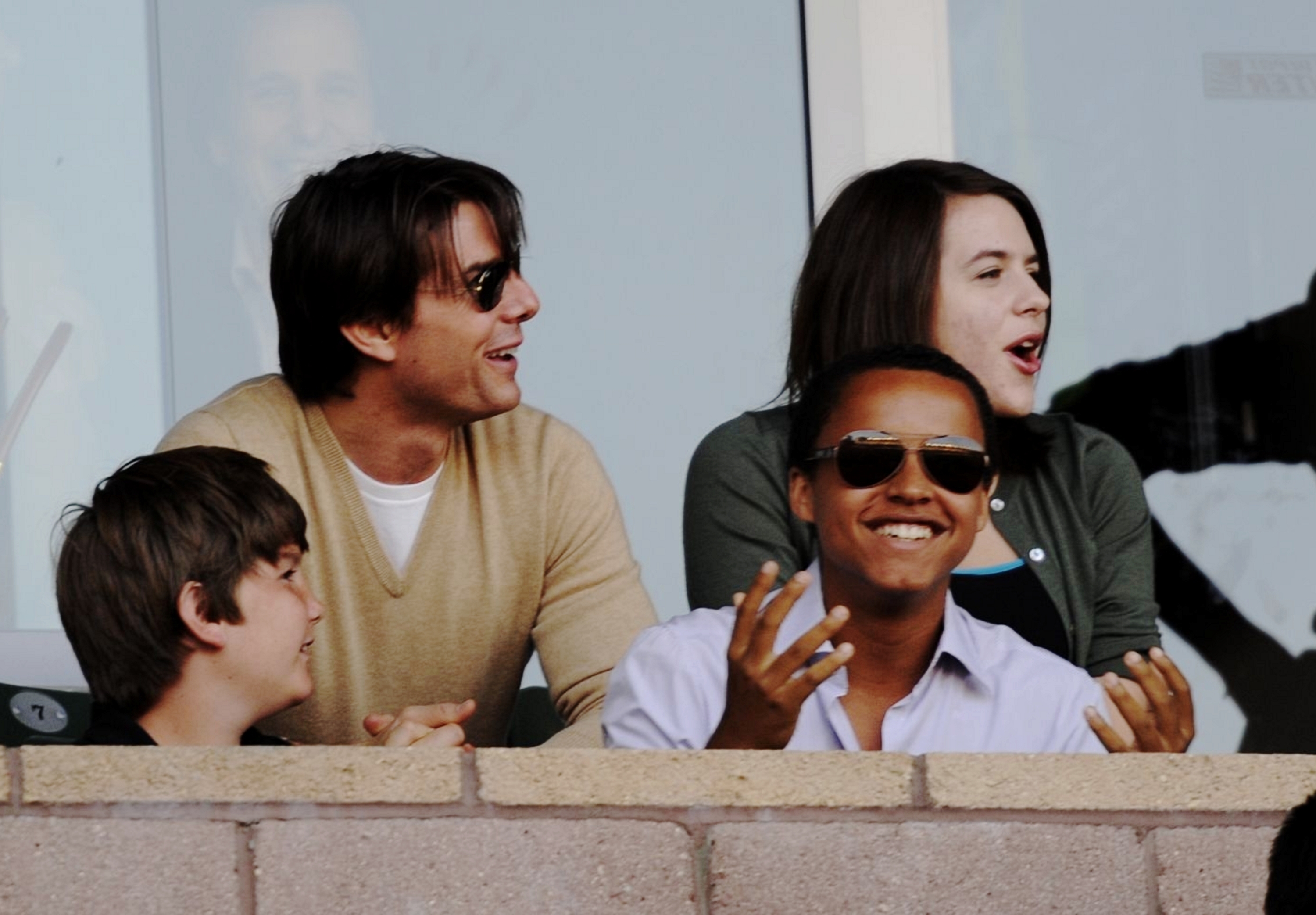 Tom Cruise enjoying a sports event with Connor and Isabella Cruise. Tom is in a casual sweater, sunglasses, and is smiling and interacting with his children