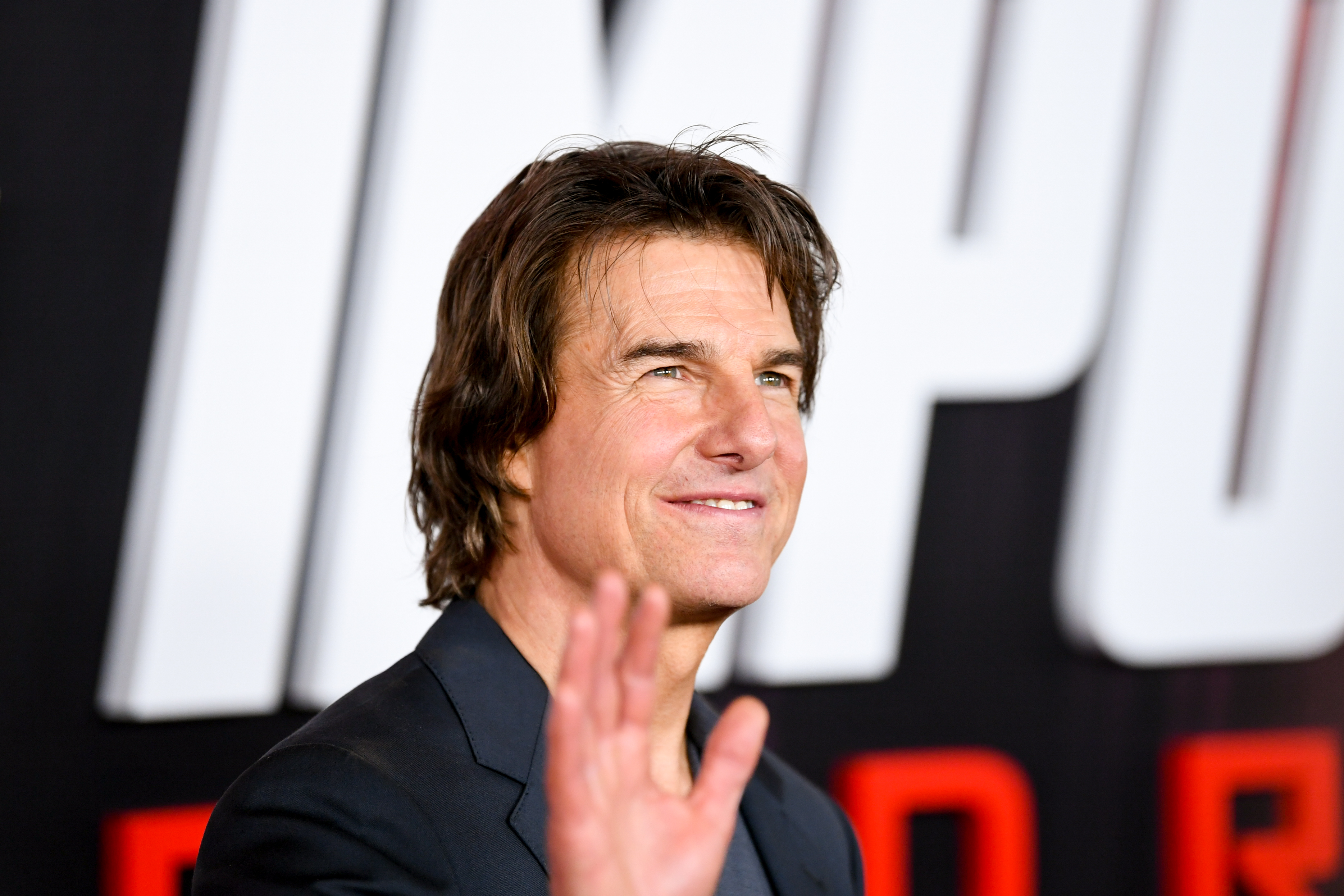 Tom Cruise waves while posing at a red carpet event