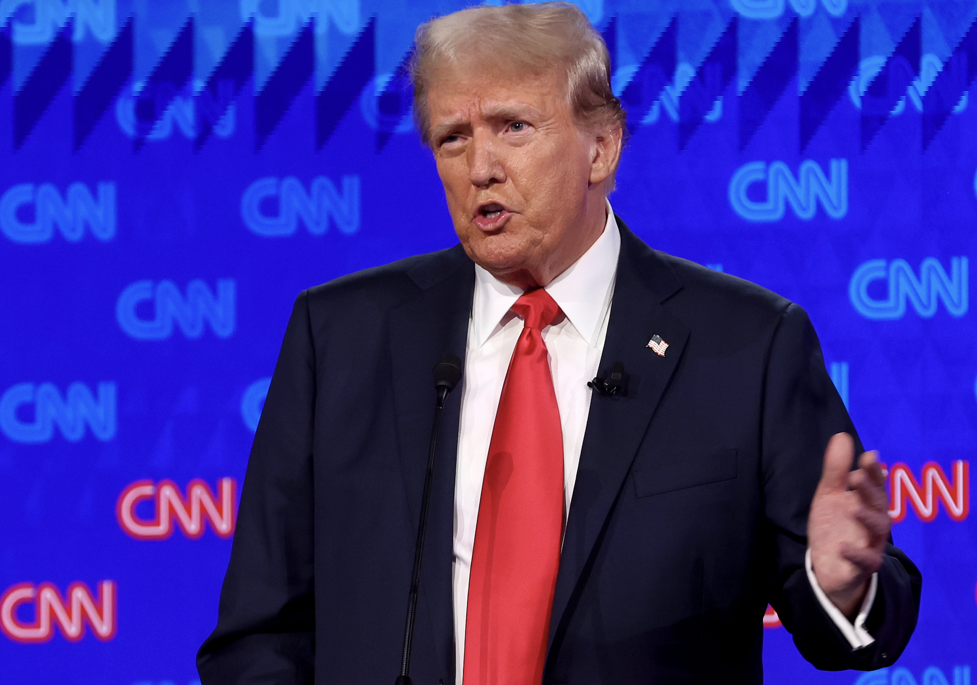 Donald Trump speaks at a CNN event, wearing a dark suit, white shirt, and red tie