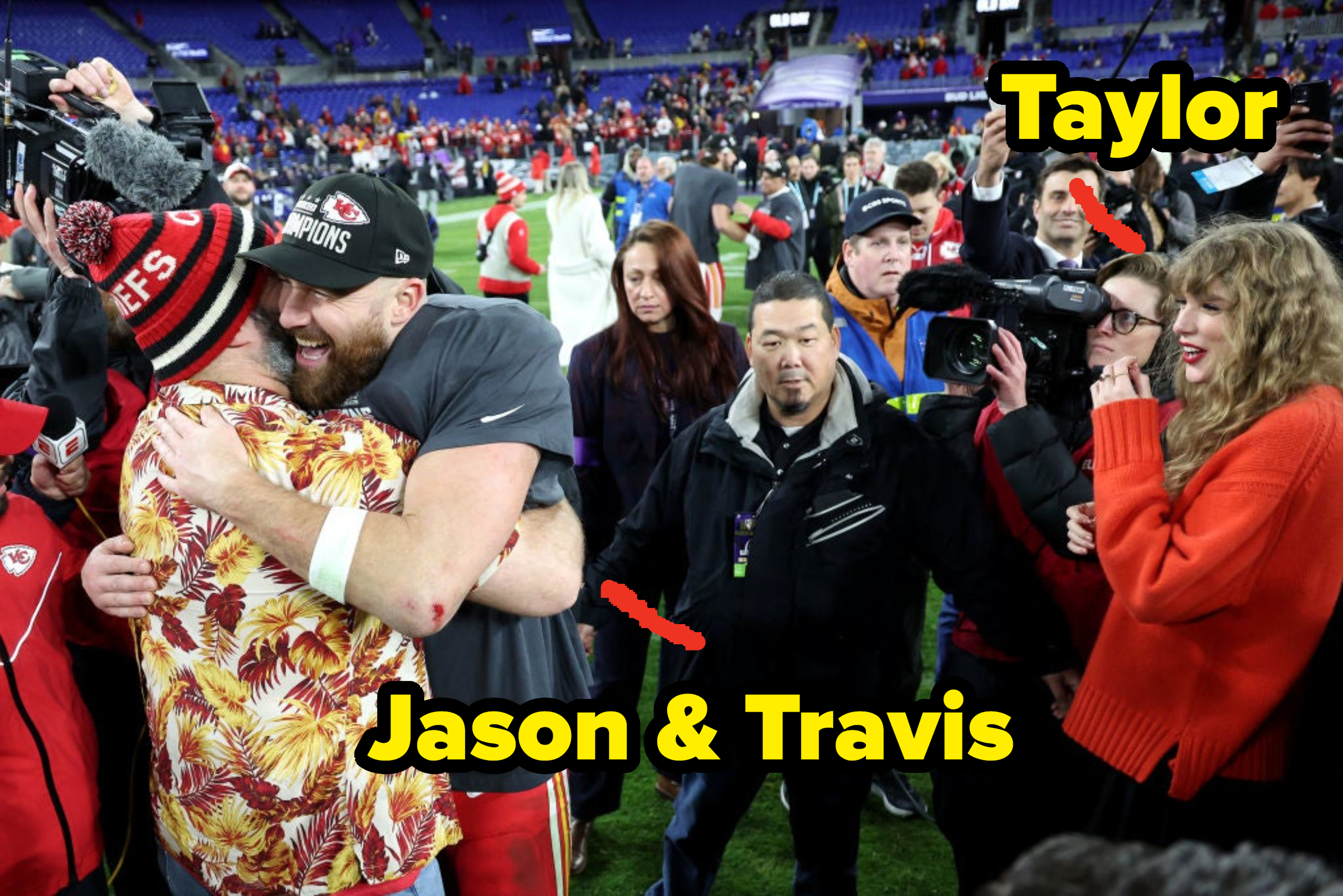 Taylor Swift smiles and watches Travis Kelce embrace a fan in a colorful shirt at a sports event. They are surrounded by photographers and fans
