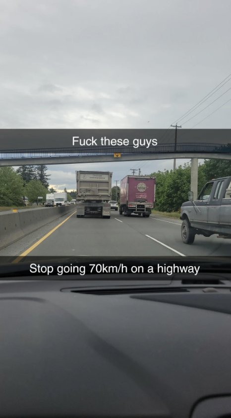 View from a car on the highway showing a white truck and a pink truck. Text overlay reads: &quot;Fuck these guys. Stop going 70km/h on a highway.&quot;