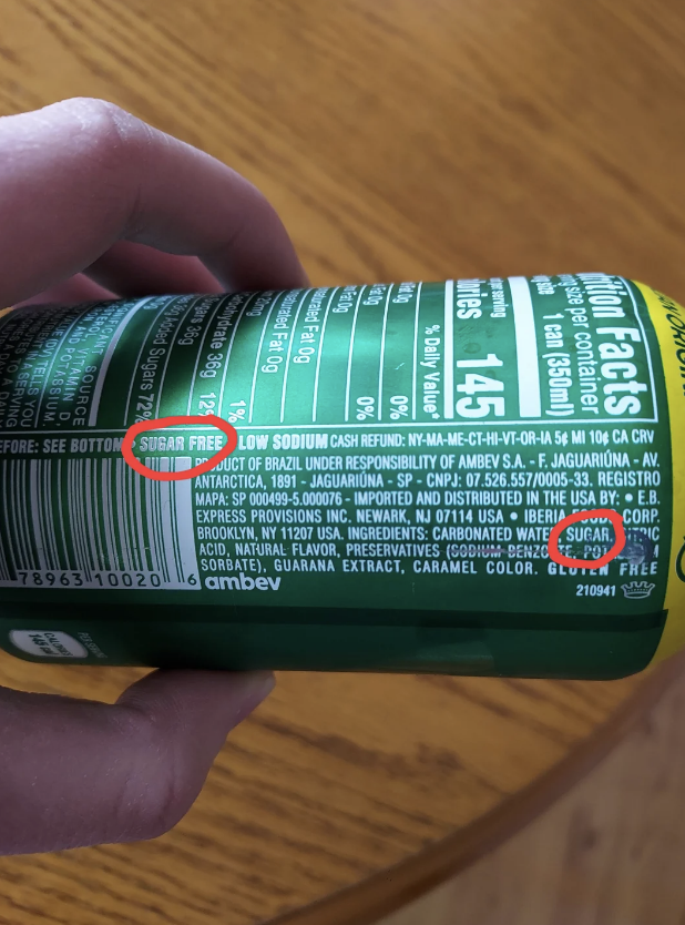 Can labeled &#x27;Sugar Free&#x27; but also lists sugar in the ingredients. Close-up of a hand holding the can