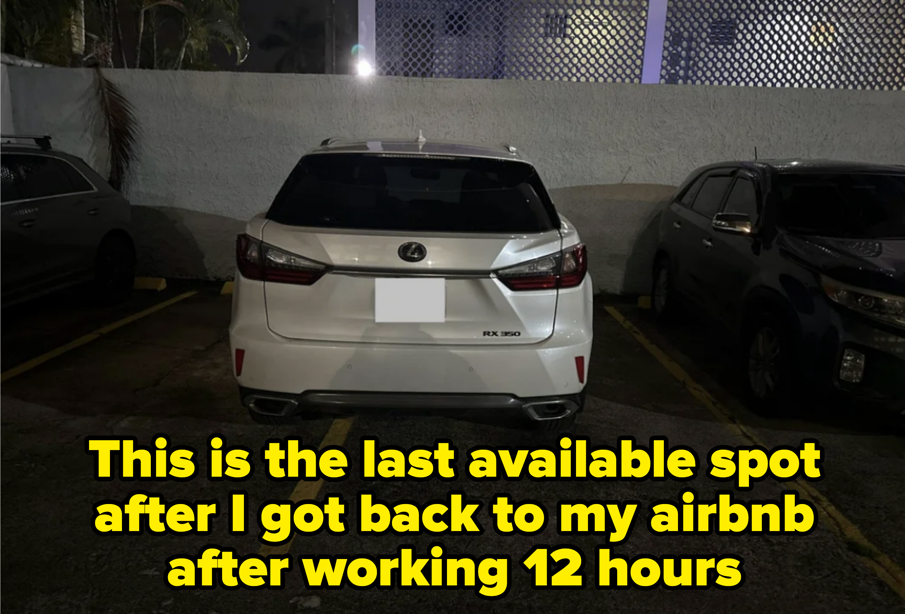 A white Lexus RX 350 is parked in a spot, slightly over the left yellow line, between two other vehicles in a dimly lit parking lot at night