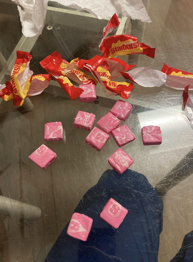 Unwrapped pink Starburst candies and their wrappers on a glass table