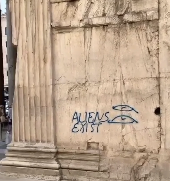 Graffiti on an ancient stone building reads &quot;ALIENS EXIST&quot; with two UFO drawings