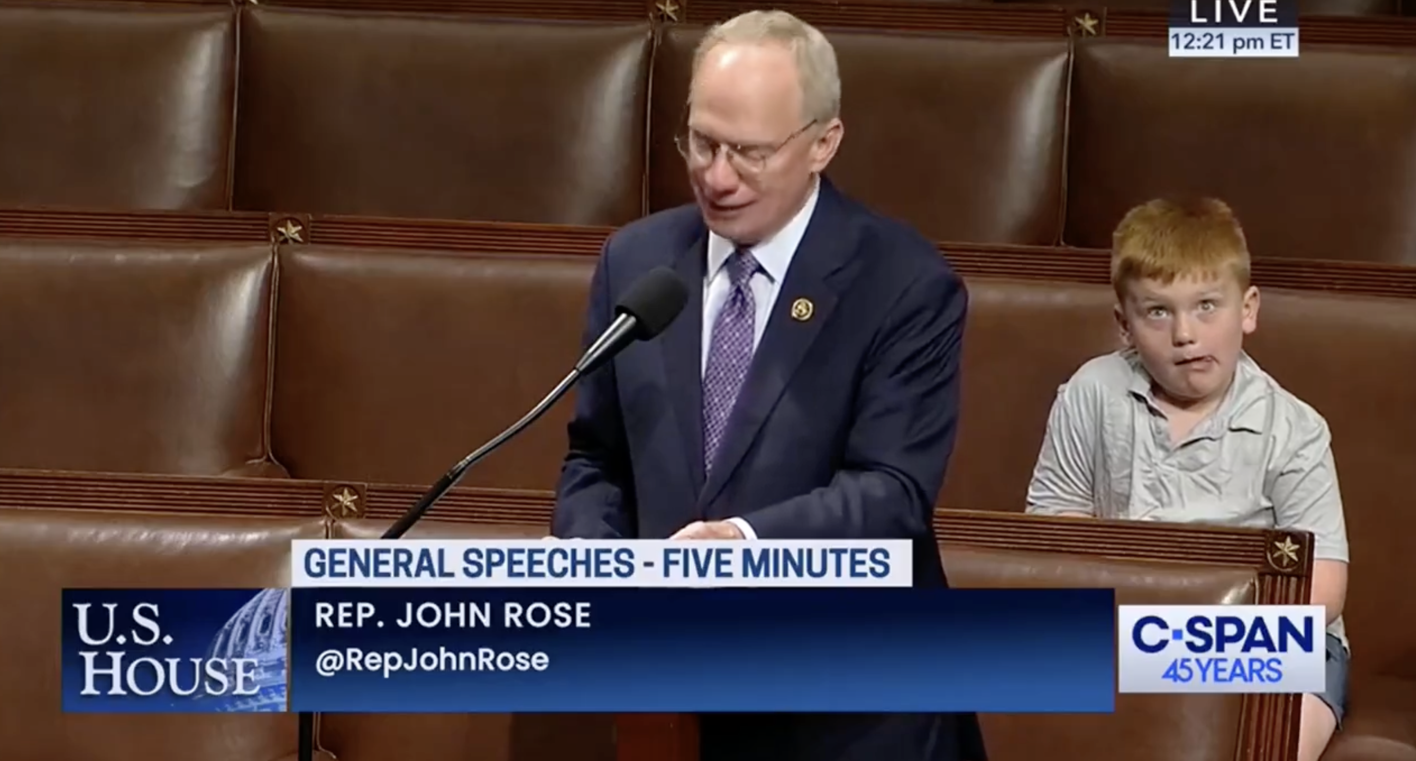 Rep. John Rose delivers a speech at the U.S. House with a young boy behind him. Content shown on C-SPAN