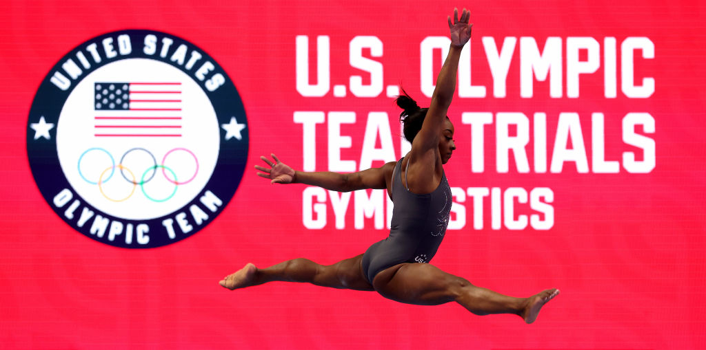 Simone Biles performs a split leap during the U.S. Olympic Team Trials for Gymnastics. The background displays the U.S. Olympic Team logo and event title