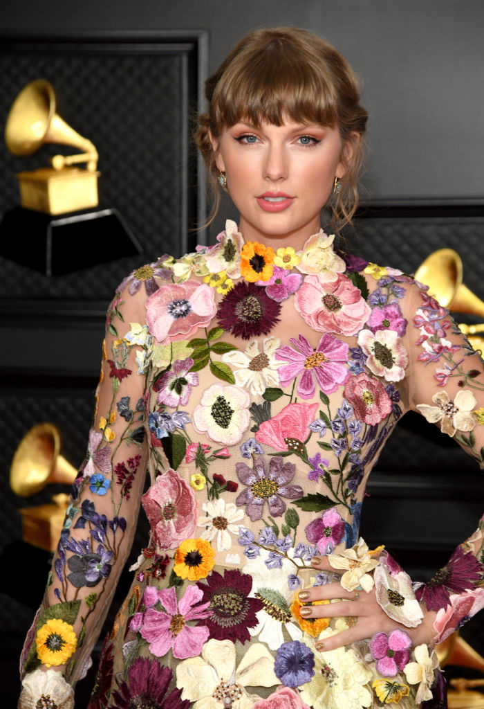 Taylor Swift on the red carpet at an event, wearing a floral-embroidered dress with various flower designs