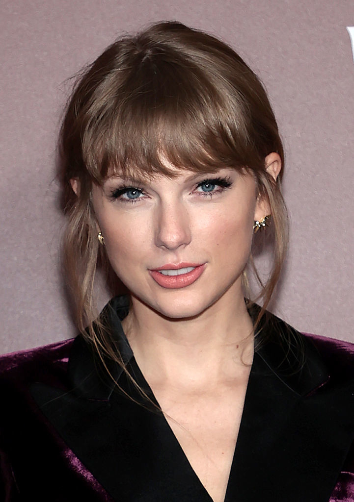 Taylor Swift with bangs, wearing a velvet jacket, poses for a photo at a formal event