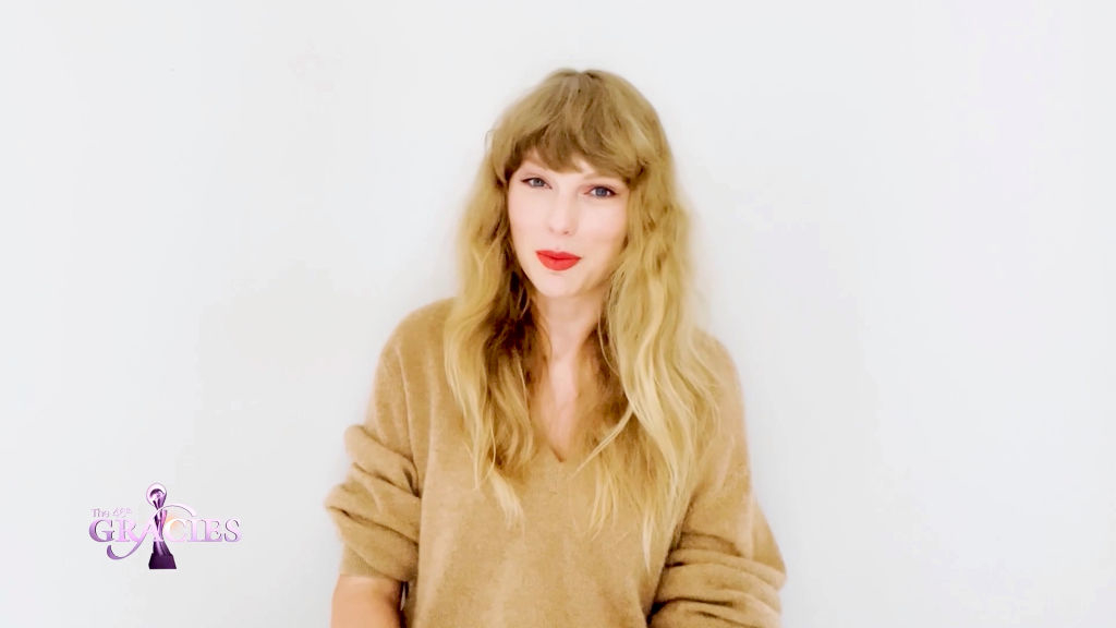 Taylor Swift smiling, wearing a casual v-neck sweater, with long hair styled naturally