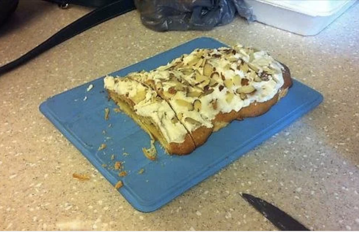 Partially eaten cake topped with sliced almonds and frosting, placed on a blue cutting board on a kitchen counter