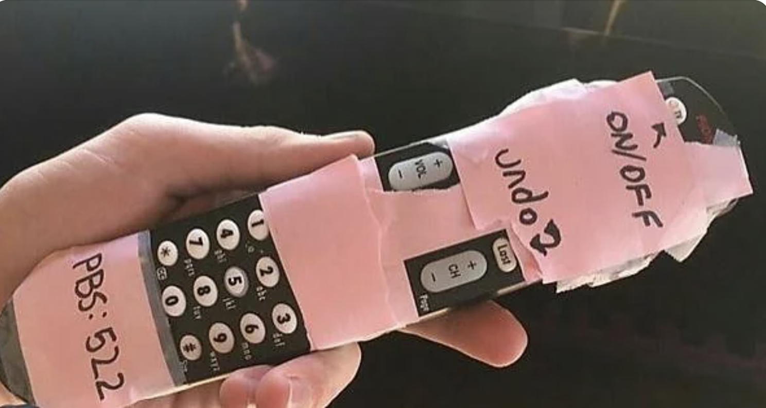 TV remote control with handwritten labels on pink tape for buttons like ON/OFF and PBS: 522, held in someone&#x27;s hand, suggesting customization for ease of use