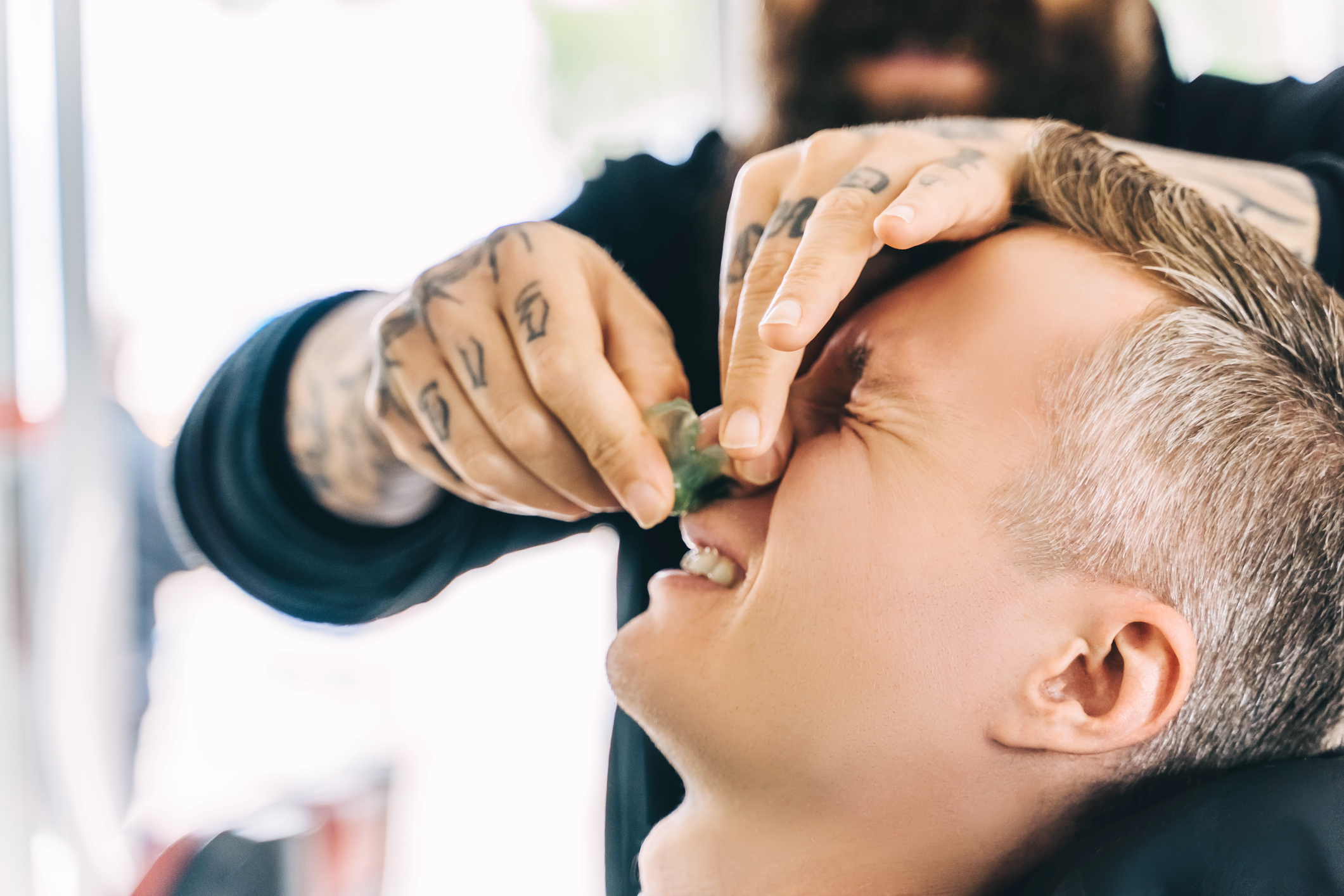 A person with visible tattoos on their hands applies a facial treatment to another person&#x27;s nose