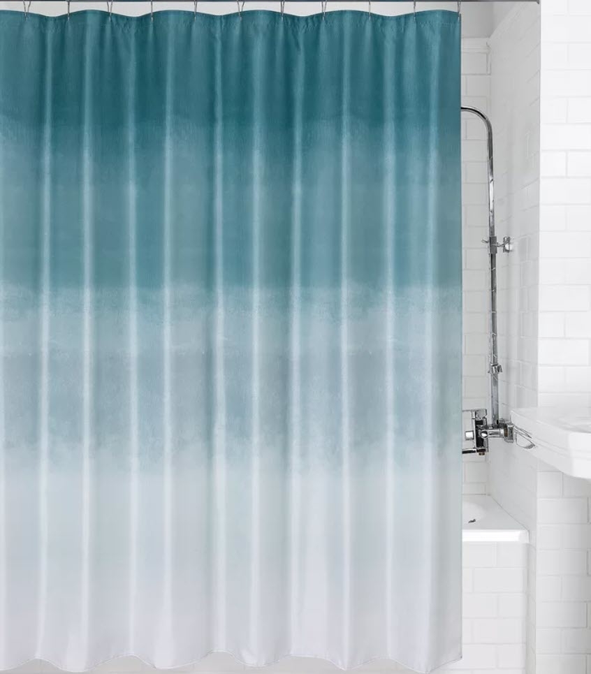 A bathroom showing a shower area with a blue and white gradient shower curtain. A white sink and tiles are visible in the background