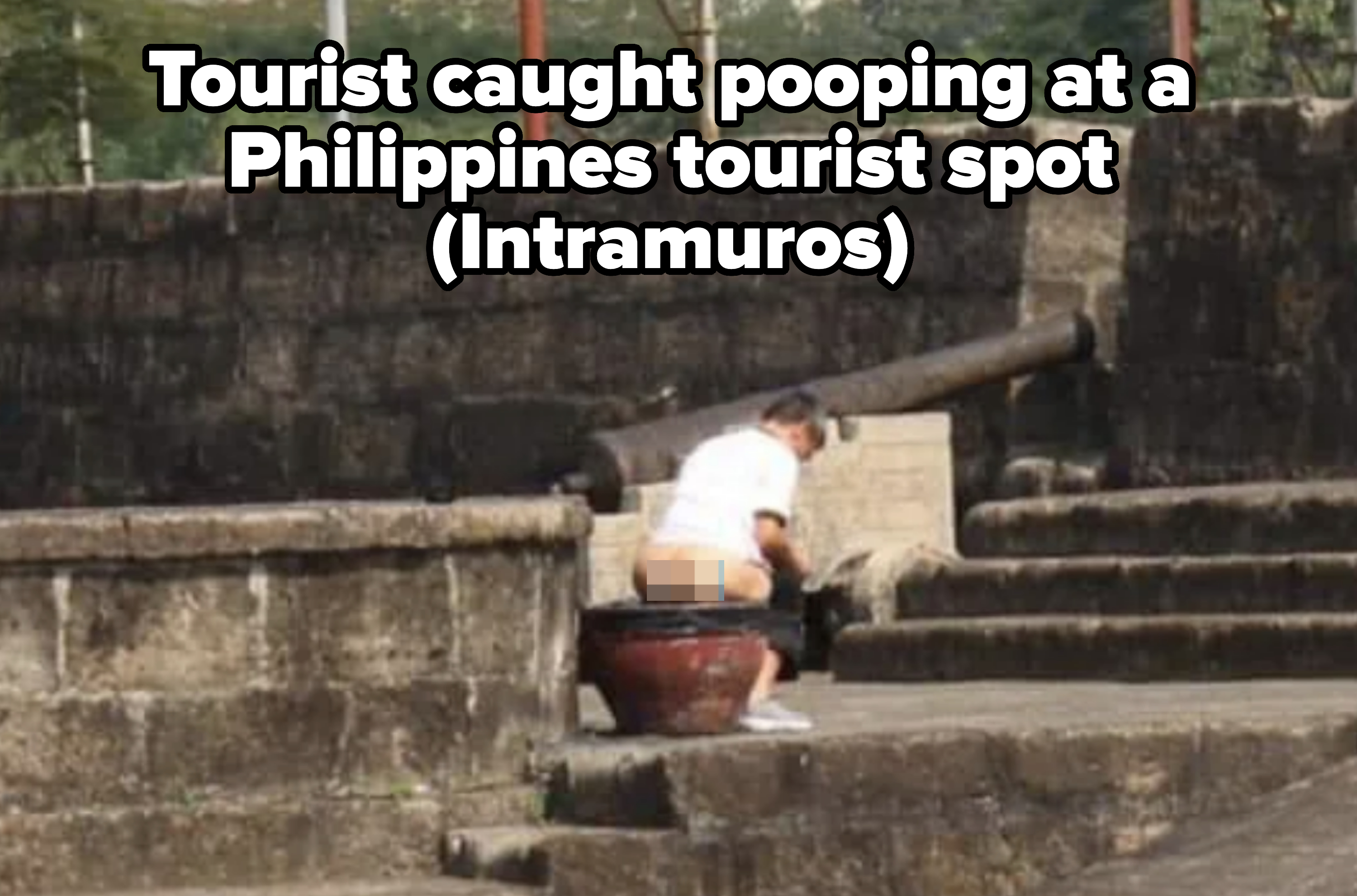 A person sits on an old, large cannon in a historic site with stone steps and walls. The person is wearing a white shirt