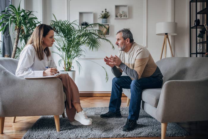 A woman and a man are sitting in chairs in a cozy living room setting, engaged in a serious conversation